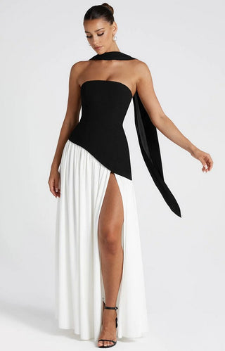 Model wearing strapless black and white maxi dress with sculpted black crepe bodice, asymmetrical hem, white chiffon skirt, high slit, and black chiffon scarf.