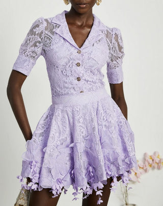 Woman wearing a lavender lace two-piece summer set with short-sleeve buttoned top and floral embroidered flared skirt, perfect for vacation or coastal getaway.