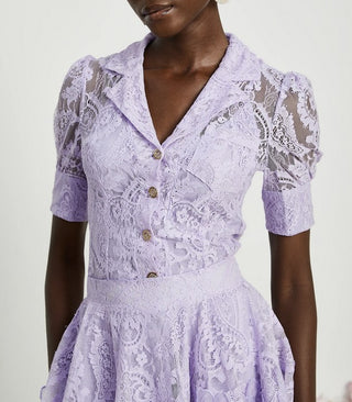 Woman wearing a lavender lace two-piece summer set with short-sleeve buttoned top and floral embroidered flared skirt, perfect for vacation or coastal getaway.