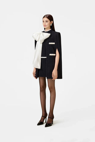 Model wearing a black and white beaded knit cape from the Desole Collection AW24 by Cielie, featuring a detachable satin bow and semi-fitted silhouette. This elegant monochrome cape coat is perfect for formal events or casual chic outfits, designed for cooler weather.
