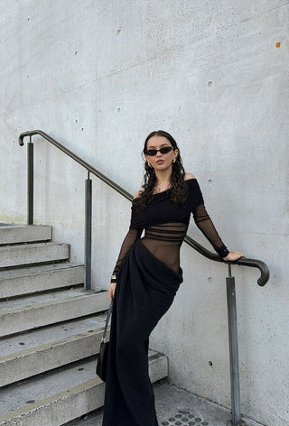 Woman in a black dress standing on concrete steps against a light gray wall.