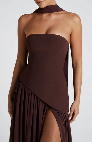 Woman in rich brown maxi dress with scarf at formal outdoor wedding setting, styled with nude heels.