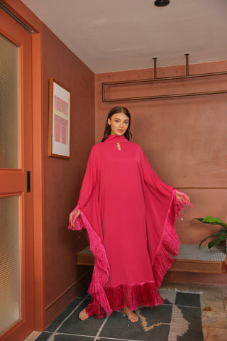 Woman in a bright pink dress standing in a room with a red wall and a plant.