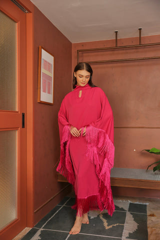 Woman in a bright pink dress with fringe standing in a room with a red wall and wooden door.