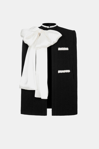 Model wearing a black and white beaded knit cape from the Desole Collection AW24 by Cielie, featuring a detachable satin bow and semi-fitted silhouette. This elegant monochrome cape coat is perfect for formal events or casual chic outfits, designed for cooler weather.