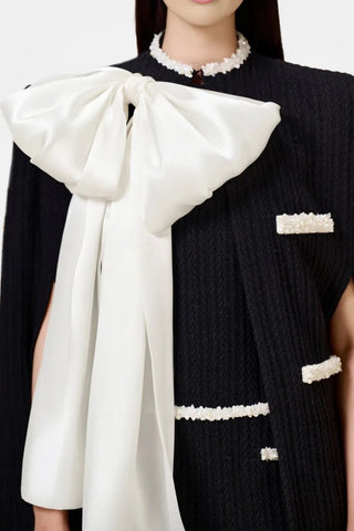 Model wearing a black and white beaded knit cape from the Desole Collection AW24 by Cielie, featuring a detachable satin bow and semi-fitted silhouette. This elegant monochrome cape coat is perfect for formal events or casual chic outfits, designed for cooler weather.