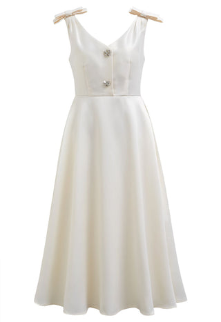 Elegant white midi dress with bow shoulder details, crystal buttons, and side pockets, perfect for bridal showers, engagement parties, rehearsal dinners, and cocktail events. A-line silhouette ideal for bridal and cocktail events. Cielie Vienna Fashion Brand Rental Gown