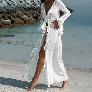 Woman walking barefoot on a beach wearing a long white mesh beach cover-up dress with ruffle sleeves and tie-front detail, perfect for summer vacations and beachwear styling. Bridal Beach Dress