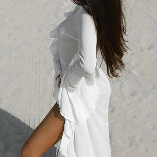 Woman walking barefoot on a beach wearing a long white mesh beach cover-up dress with ruffle sleeves and tie-front detail, perfect for summer vacations and beachwear styling.