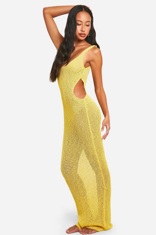 Woman in yellow knit maxi dress with drink, standing by beachside railing under palm trees.