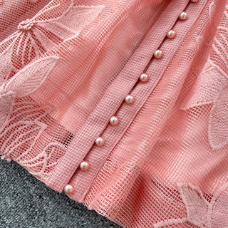 Close-up of a pink lace fabric with pearl embellishments on a gray surface.