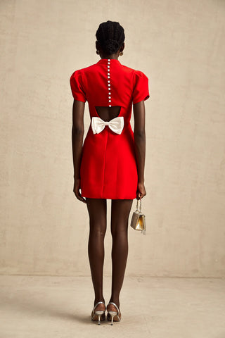 Back view of a red holiday dress featuring pearl button closure, a white bow detail, and an elegant cut-out design.