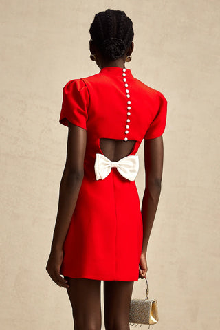 Back view of a red holiday dress featuring pearl button closure, a white bow detail, and an elegant cut-out design.