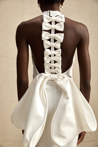 A sophisticated model wearing the Serinay White Oversize-Bow Bandage Dress, featuring a sleek sleeveless design, a round neckline, and an oversized bow detail at the back. The maxi-length dress includes an open back, a rear slit, and a sculpting bandage fit, perfect for bridal events, engagement parties, and wedding rehearsals.