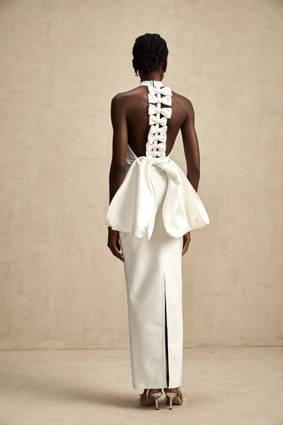 A sophisticated model wearing the Serinay White Oversize-Bow Bandage Dress, featuring a sleek sleeveless design, a round neckline, and an oversized bow detail at the back. The maxi-length dress includes an open back, a rear slit, and a sculpting bandage fit, perfect for bridal events, engagement parties, and wedding rehearsals.