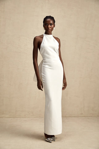 A sophisticated model wearing the Serinay White Oversize-Bow Bandage Dress, featuring a sleek sleeveless design, a round neckline, and an oversized bow detail at the back. The maxi-length dress includes an open back, a rear slit, and a sculpting bandage fit, perfect for bridal events, engagement parties, and wedding rehearsals.