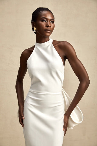 A sophisticated model wearing the Serinay White Oversize-Bow Bandage Dress, featuring a sleek sleeveless design, a round neckline, and an oversized bow detail at the back. The maxi-length dress includes an open back, a rear slit, and a sculpting bandage fit, perfect for bridal events, engagement parties, and wedding rehearsals.