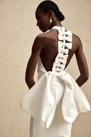 A sophisticated model wearing the Serinay White Oversize-Bow Bandage Dress, featuring a sleek sleeveless design, a round neckline, and an oversized bow detail at the back. The maxi-length dress includes an open back, a rear slit, and a sculpting bandage fit, perfect for bridal events, engagement parties, and wedding rehearsals.