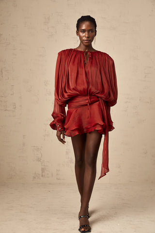 Model wearing the Evelyn Red Draped Mini Dress with a pleated design, long buttoned-cuff sleeves, neck tie fastening, and a twist detail at the waist. The dress features a ruffled hem, perfect for festive occasions like Christmas, autumn gatherings, or spring celebrations. Cielie