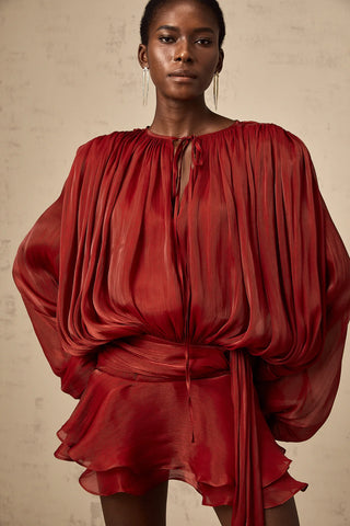 Model wearing the Evelyn Red Draped Mini Dress with a pleated design, long buttoned-cuff sleeves, neck tie fastening, and a twist detail at the waist. The dress features a ruffled hem, perfect for festive occasions like Christmas, autumn gatherings, or spring celebrations. Cielie