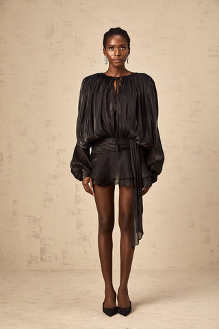 Model wearing the Evelyn Black Draped Mini Dress, showcasing the fully pleated design, twist waist detail, and elegant long buttoned-cuff sleeves.Black Little Dress Ruffled Mini Longsleeve