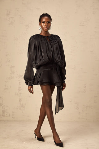 Model wearing the Evelyn Black Draped Mini Dress, showcasing the fully pleated design, twist waist detail, and elegant long buttoned-cuff sleeves.Black Little Dress Ruffled Mini Longsleeve