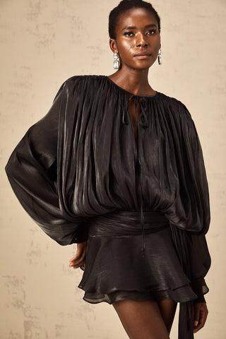 Model wearing the Evelyn Black Draped Mini Dress, showcasing the fully pleated design, twist waist detail, and elegant long buttoned-cuff sleeves.Black Little Dress Ruffled Mini Longsleeve