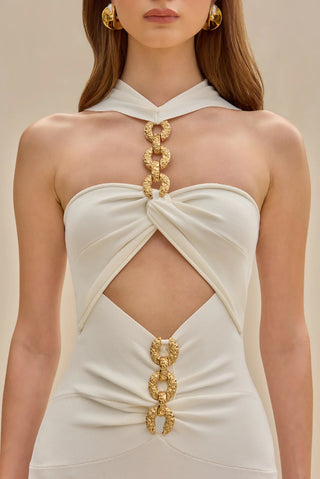 White knit midi dress with gold chain embellishments, bold cutouts, and a halter neckline.