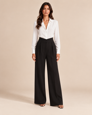A woman modeling a white long-sleeve collared blouse tucked into high-waisted black wide-leg trousers, standing against a plain beige studio background.