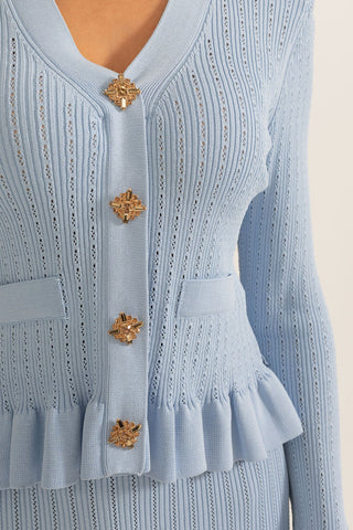 Light blue knitted cardigan with decorative buttons on a beige background
