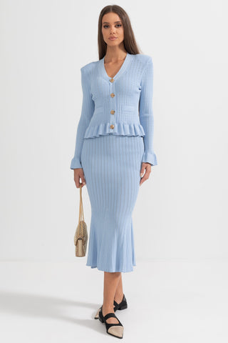 Woman wearing a light blue knit outfit with a cardigan and skirt on a white background