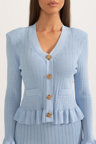 Light blue knit cardigan with ruffled details and gold buttons on a white background