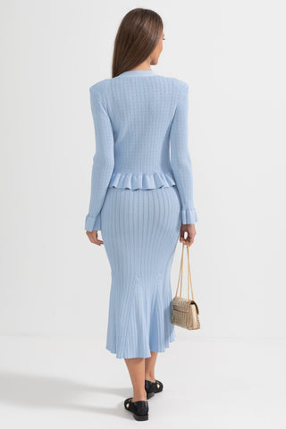 Woman wearing a light blue ribbed dress with a peplum waist on a white background