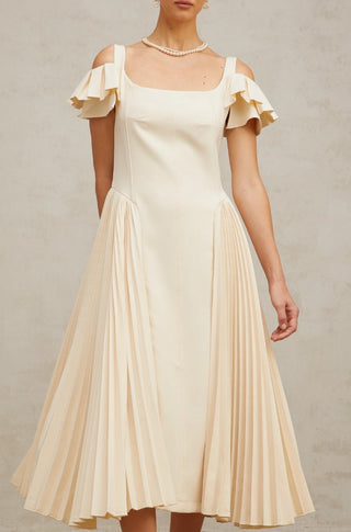 Woman wearing a neutral pleated midi dress with flutter sleeves and darted bodice, ideal for elegant summer events, wedding guest looks, or garden parties.