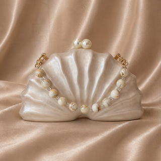 Shell-shaped handbag with pearl necklace on a beige fabric background