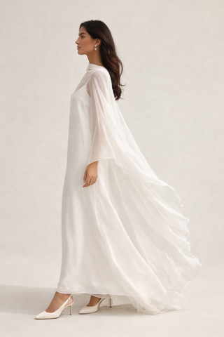 Woman wearing a white dress with a cape against a plain background