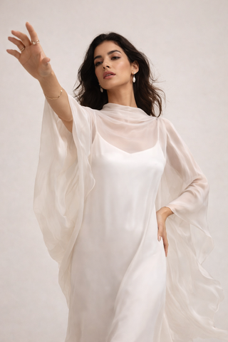 Woman wearing a white outfit with a flowing shawl against a plain background