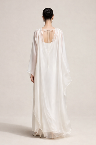 Person wearing a flowing white dress with a plain background Cape Dress