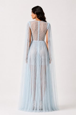 A model shown from the back wearing a light blue lace and tulle gown with long sheer cape sleeves and a sheer back panel, photographed against a plain light gray studio background.