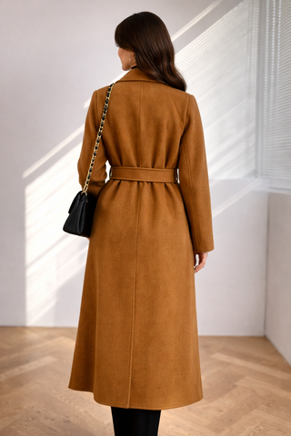 Woman wearing a brown coat in a minimalistic room with a black handbag.
