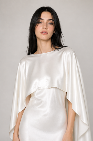 Woman wearing a white satin cape against a plain background