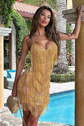 Woman in a gold beaded dress standing by a poolside.