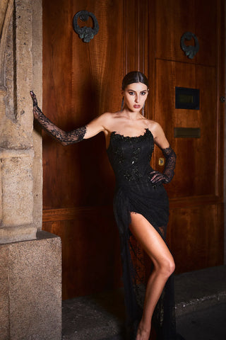 Woman in a black dress with long gloves standing in front of a wooden door.