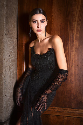Woman in a black lace dress and gloves against a wooden wall.