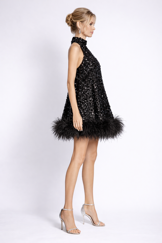 Woman wearing a black sequin dress with feather details on a white background