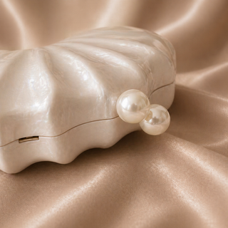 Pearl earrings in a shell-shaped jewelry box on a beige fabric background
