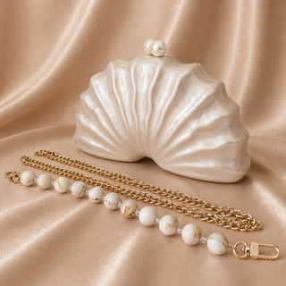 Shell-shaped handbag with pearl and chain detail on a beige fabric background