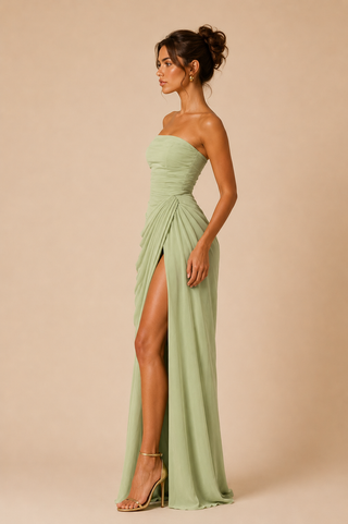 Woman wearing a strapless green wedding guest dress gown with a high slit on a beige background