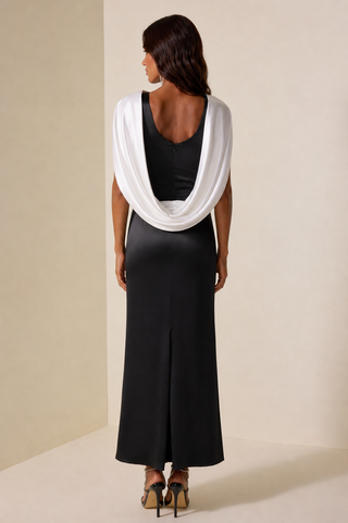 Woman wearing a black dress with a white scarf draped over her shoulders against a beige background