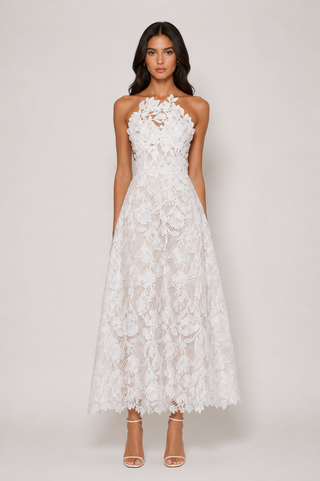 A woman modeling a strapless white lace maxi dress with a fitted bodice, floral lace overlay, and full skirt, paired with clear high-heeled sandals against a light gray studio background.